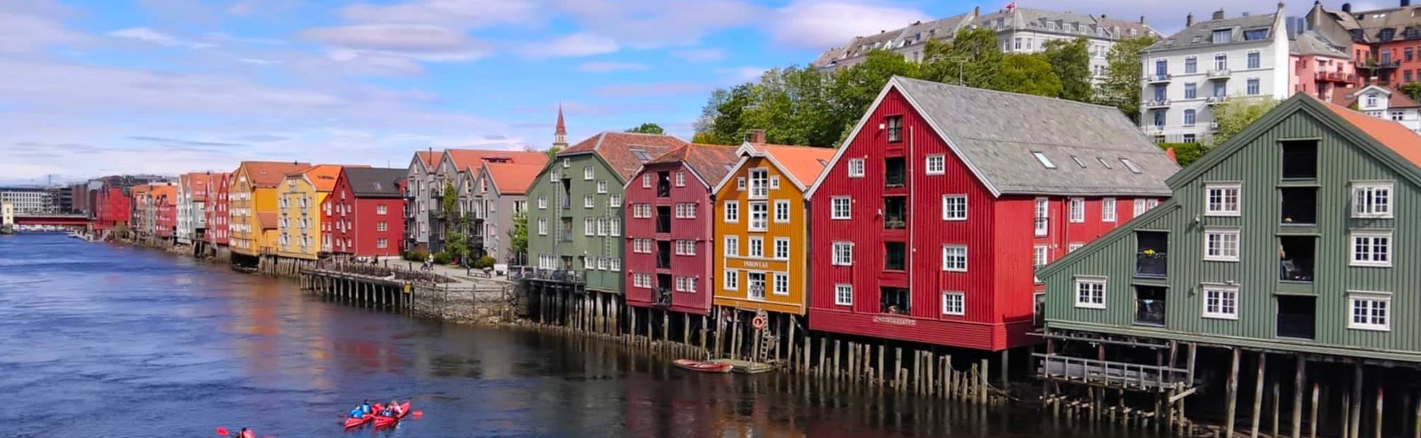 Colorful houses along the river Nid in Trondheim with a blue sky, trees and sunshine. Picture taken during a guided tour of the city center.